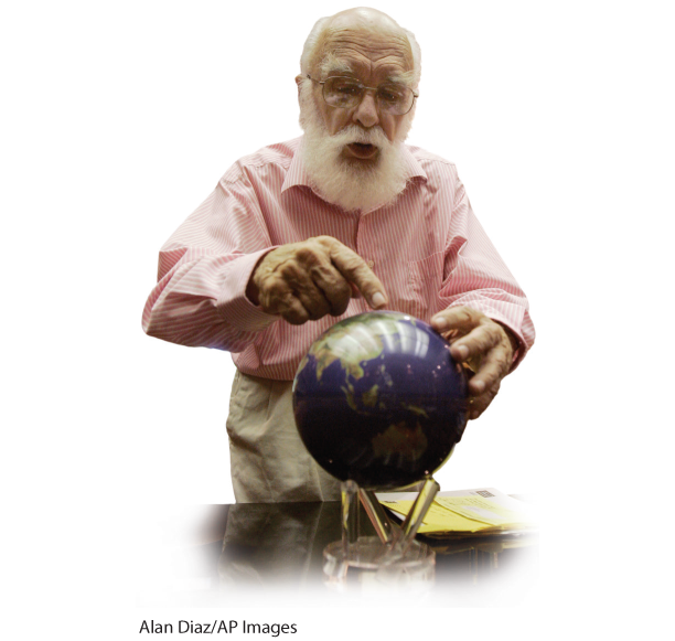 A photo shows James Randi pointing toward a point on a globe.