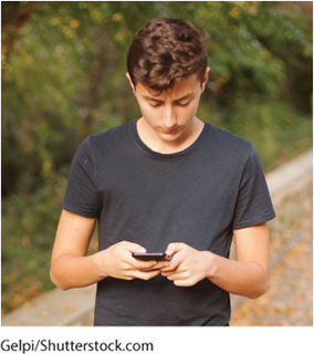 A photo shows a teenage boy looking at his phone.