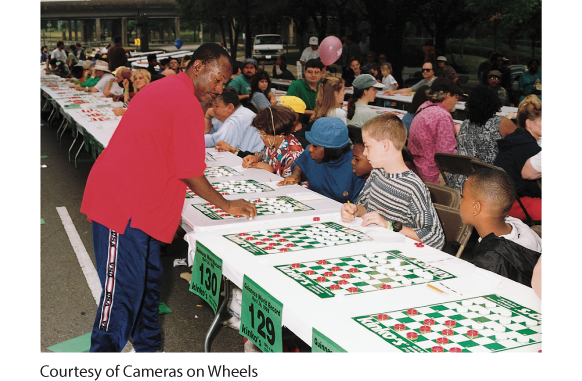 This photo shows Ron “Suki” King, the World Checkers Champion, playing checkers with one of the 385 opponents while several others are seated at long tables waiting their turns.