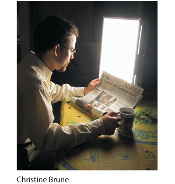 A photo of a man reading a newspaper and having coffee in front of a light box.