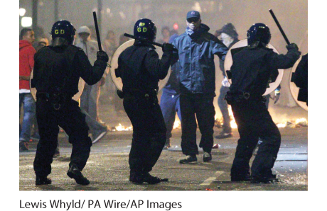 Photograph of the 2011 riots in England. There is a protester confronting three policemen in the street.