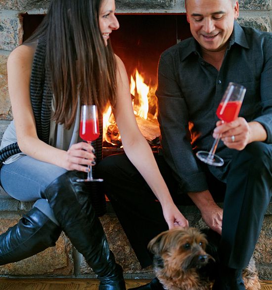 Two people sitting in front of a fireplace with bright red drinks in their hands