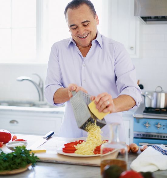 A man happily shredding a block of white cheese on a box grater