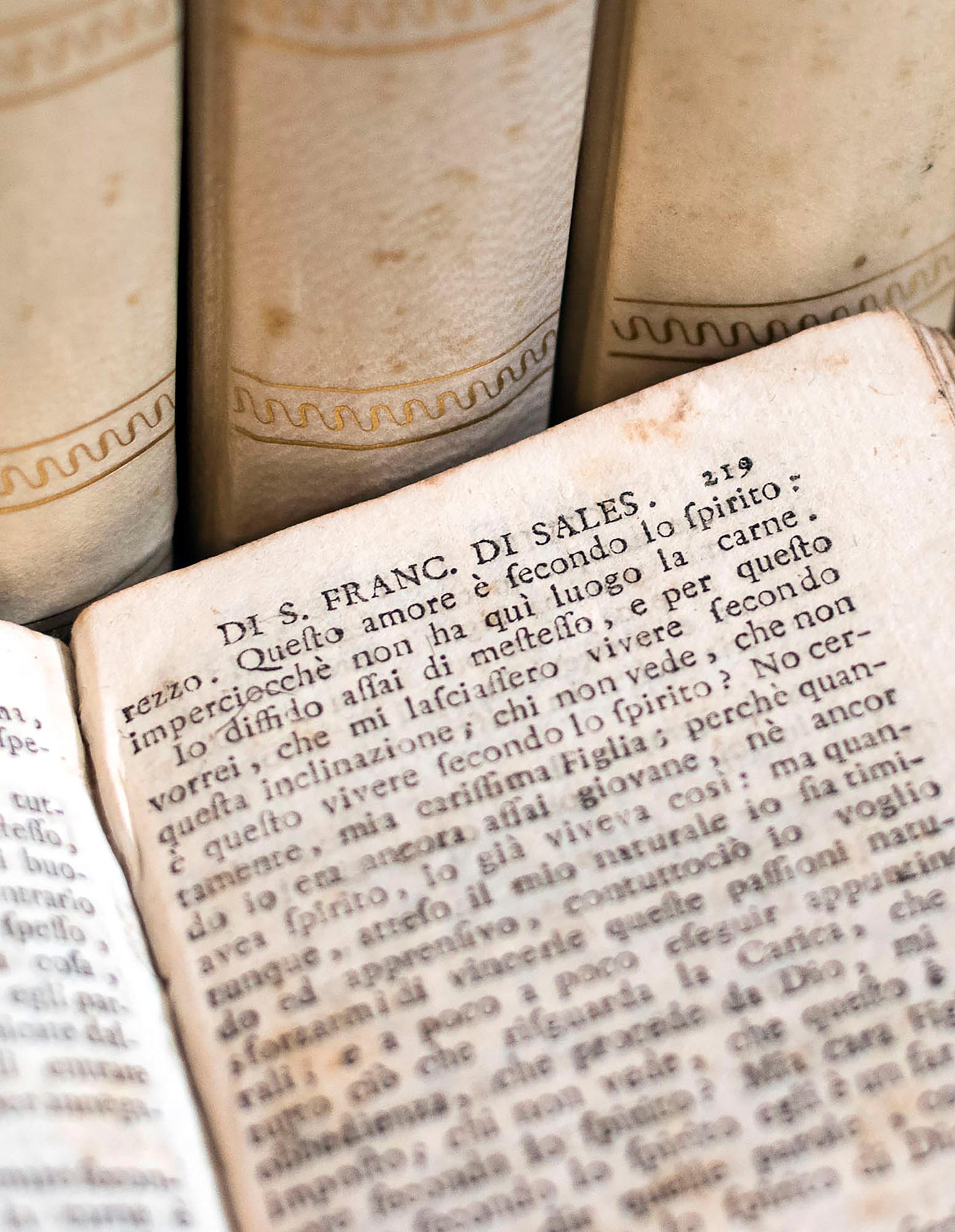 Photo of aged-looking Italian text with cream-and-gold leather book spines in the background.