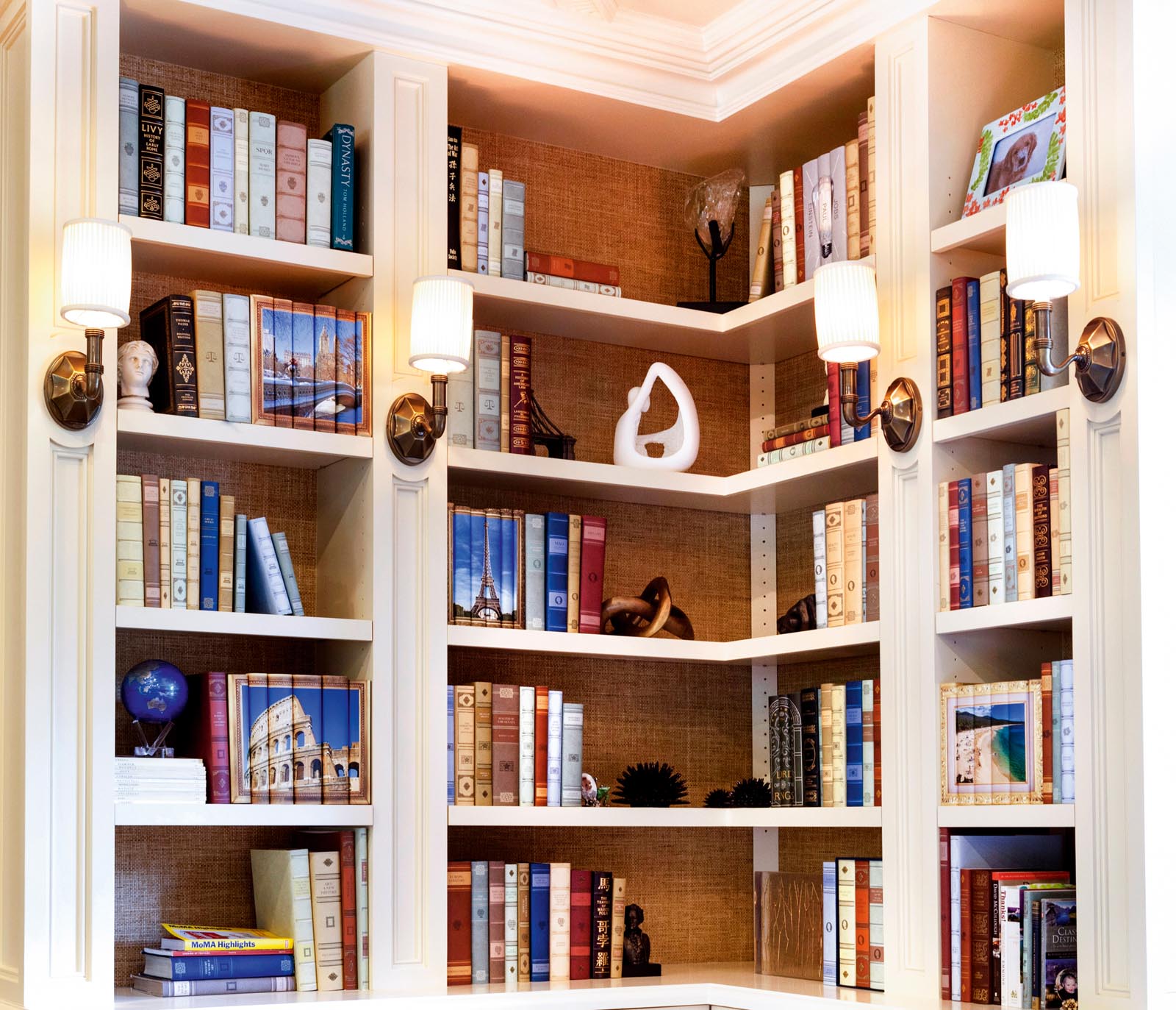 Photo of a set of shelves featuring leather-bound volumes, groups of jacketed books, and art objects.