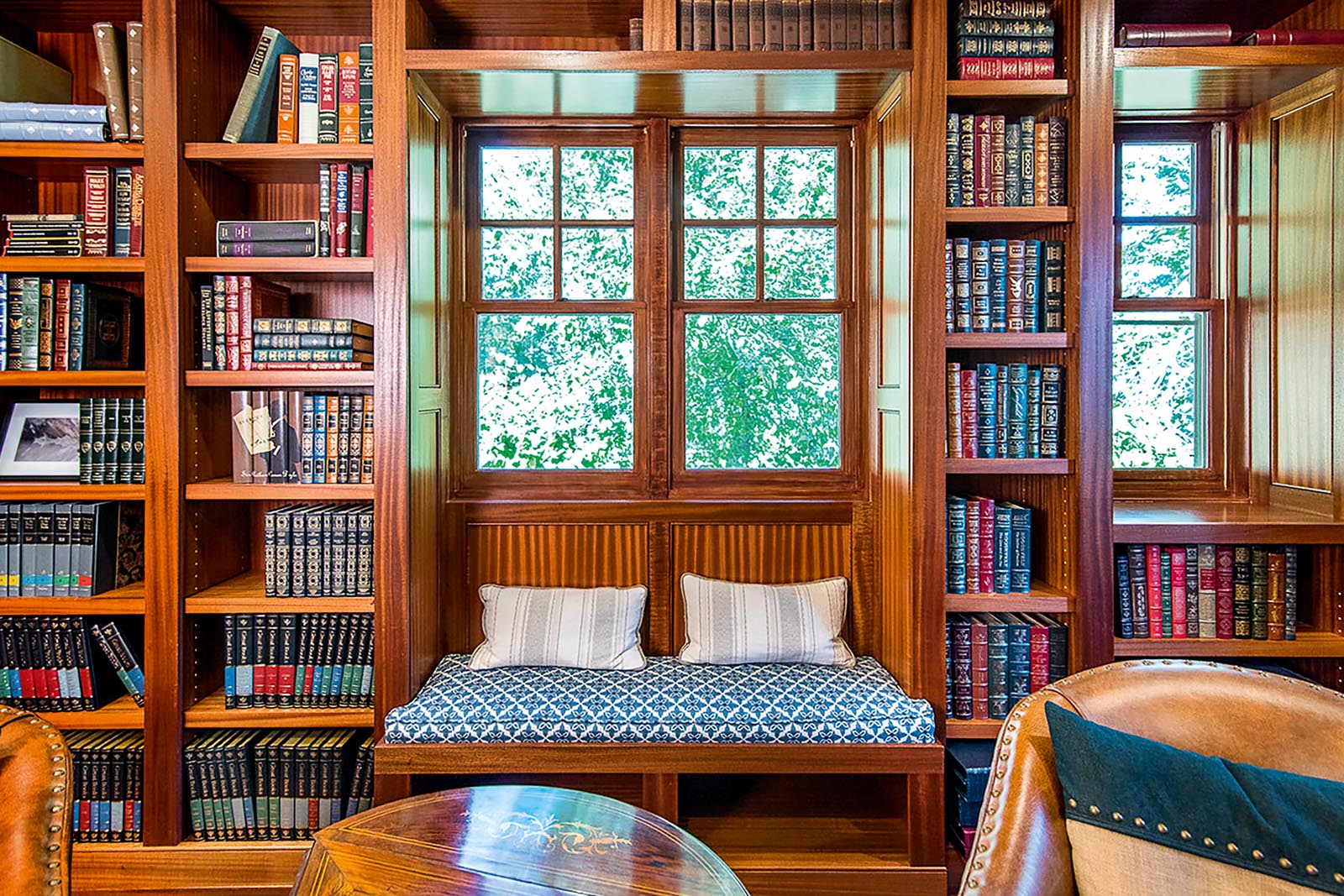 Photo of a window seat in a library with shelves of leather-bound books.