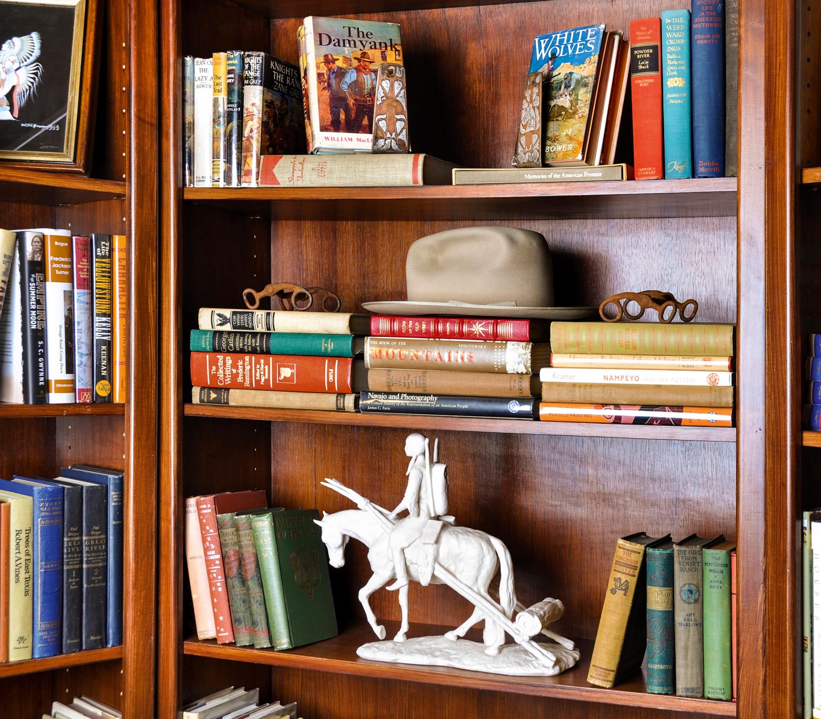 Photo of wood-paneled shelves with groups of books and Western collectibles.