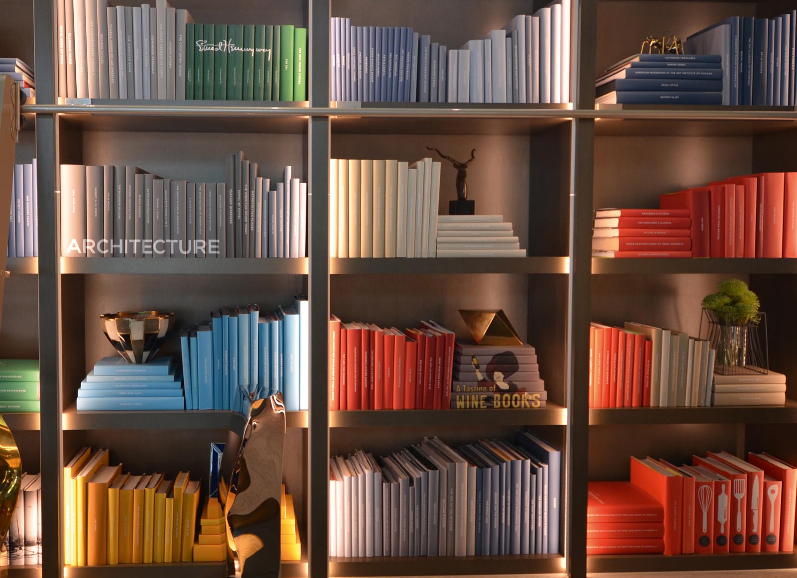 Photo of groups of books on similar subjects in similar-colored jackets, placed together on library shelves.