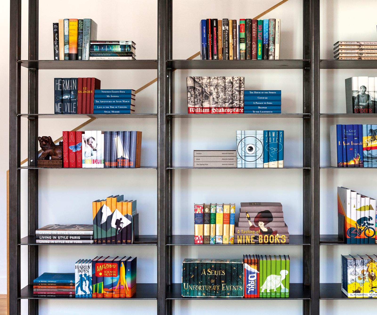 Photo of metal open-back shelved wiht groups of books, many of which have custom jackets and images spreading across multiple spines.