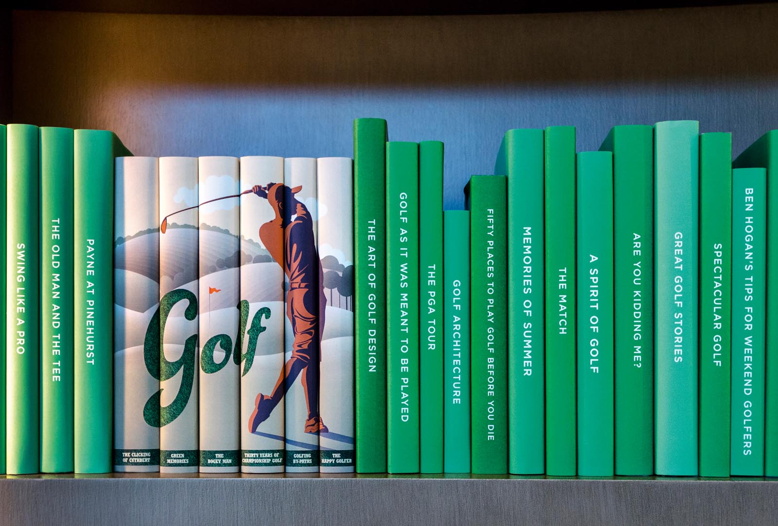 Photo of a shelf of books with custom jackets, mostly green but with one group showing the image of a man golfing.