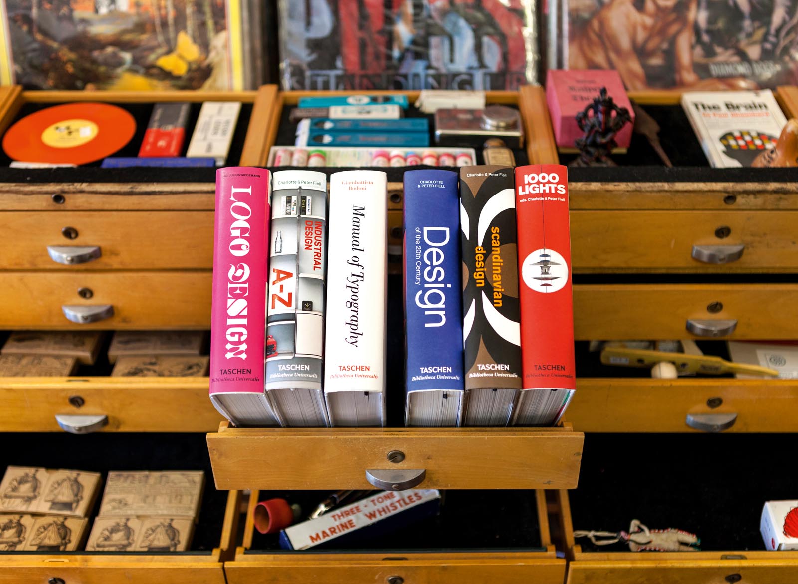 Photo of shallow drawers of collectibles, including a group of design books propped on an open drawer.