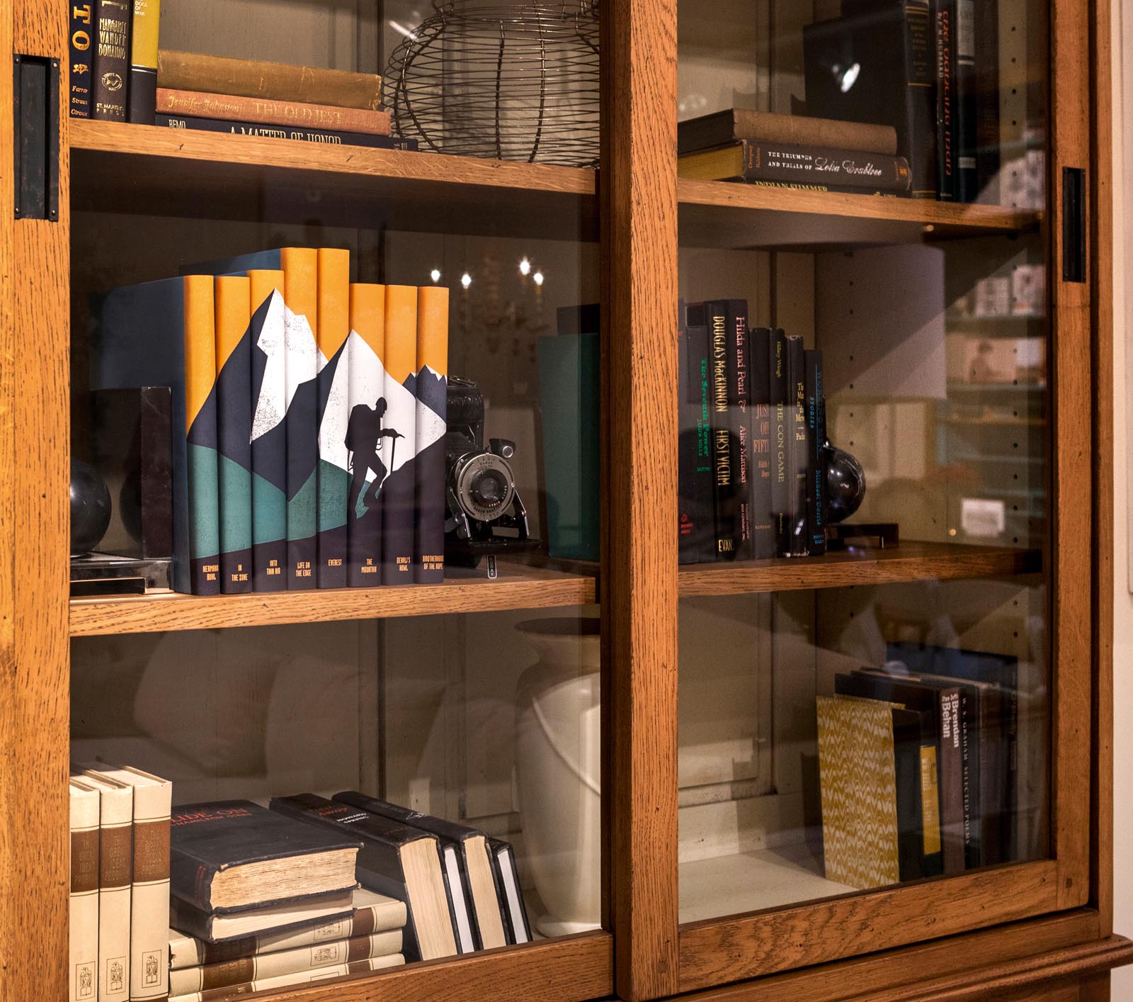 Photo of a glass-front cabinet with groups of books and other items, including a set showing a hiker and mountains.