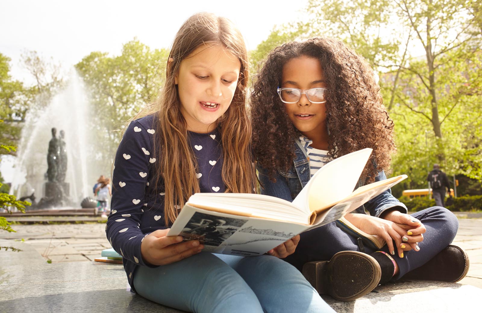 Photo of friends sharing a book in a plaza.