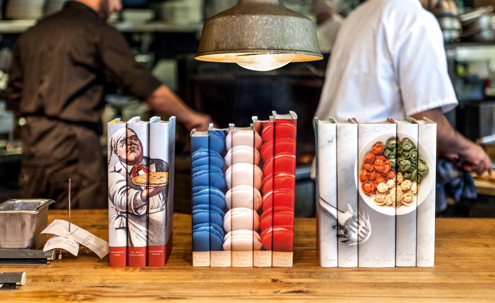 Photo of cookbook collections with custom jackets featuring food imagery in a restaurant kitchen.