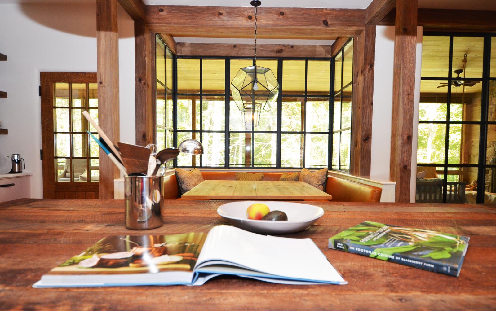 Photo of cookbooks, a fruit bowl, and utensils on a wooden counter.