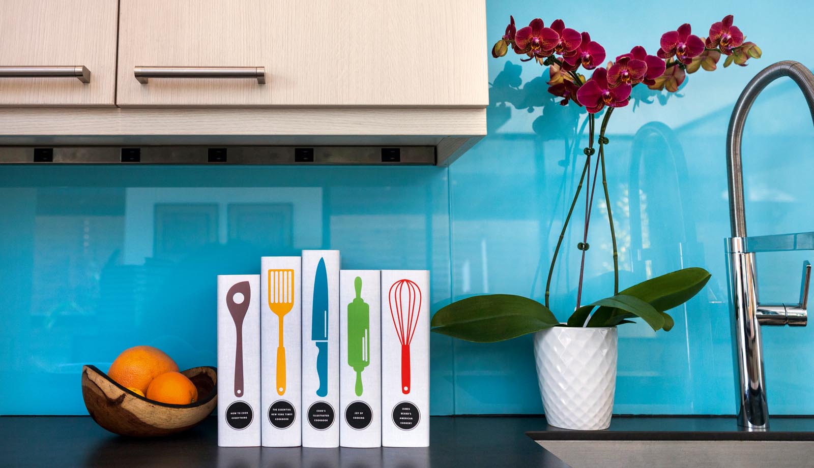 Photo of custom jacketed cookbooks featuring colorful utensils in frontof a blue backsplash.