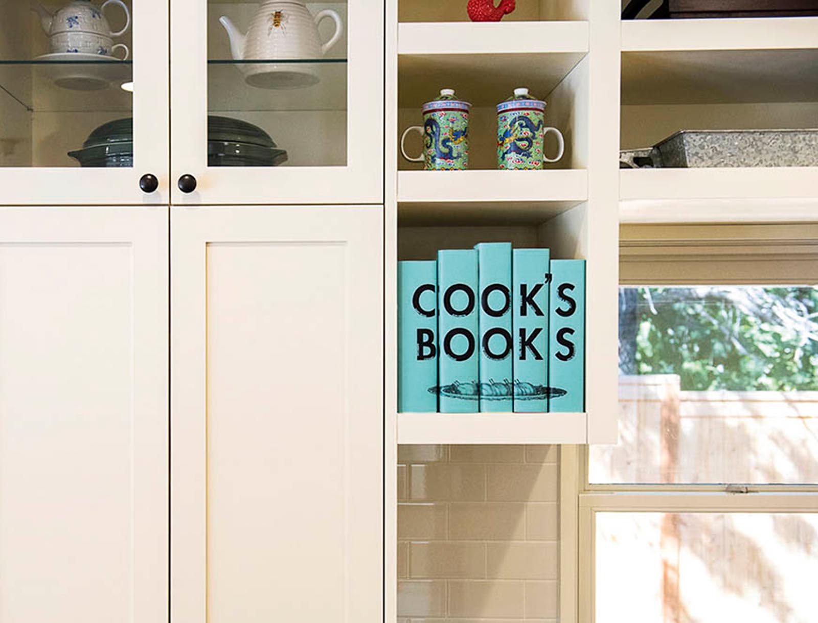 Photo of shelves around a kitchen window with a collection of servingware and a collection labeled Cook's Books.