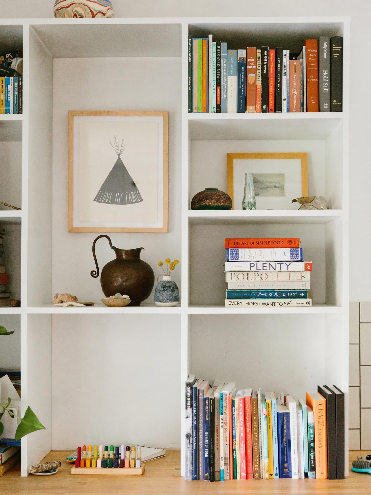 Photo of art and book collections on white shelves above a wood counter.