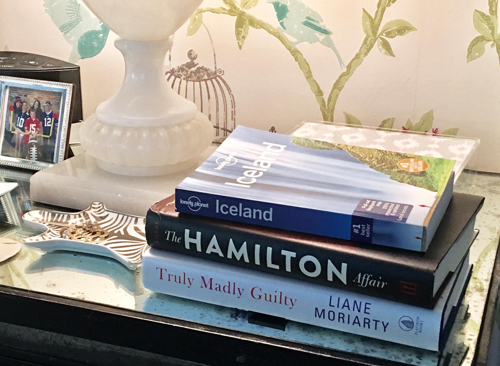 Photo of a short stack of books next to a jewelry tray and lamp and other decorative items.