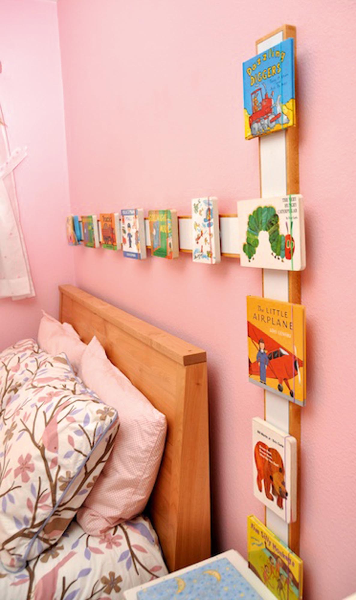 Photo of board books and small picture books on a magnetic frame above and beside a girl's bed.