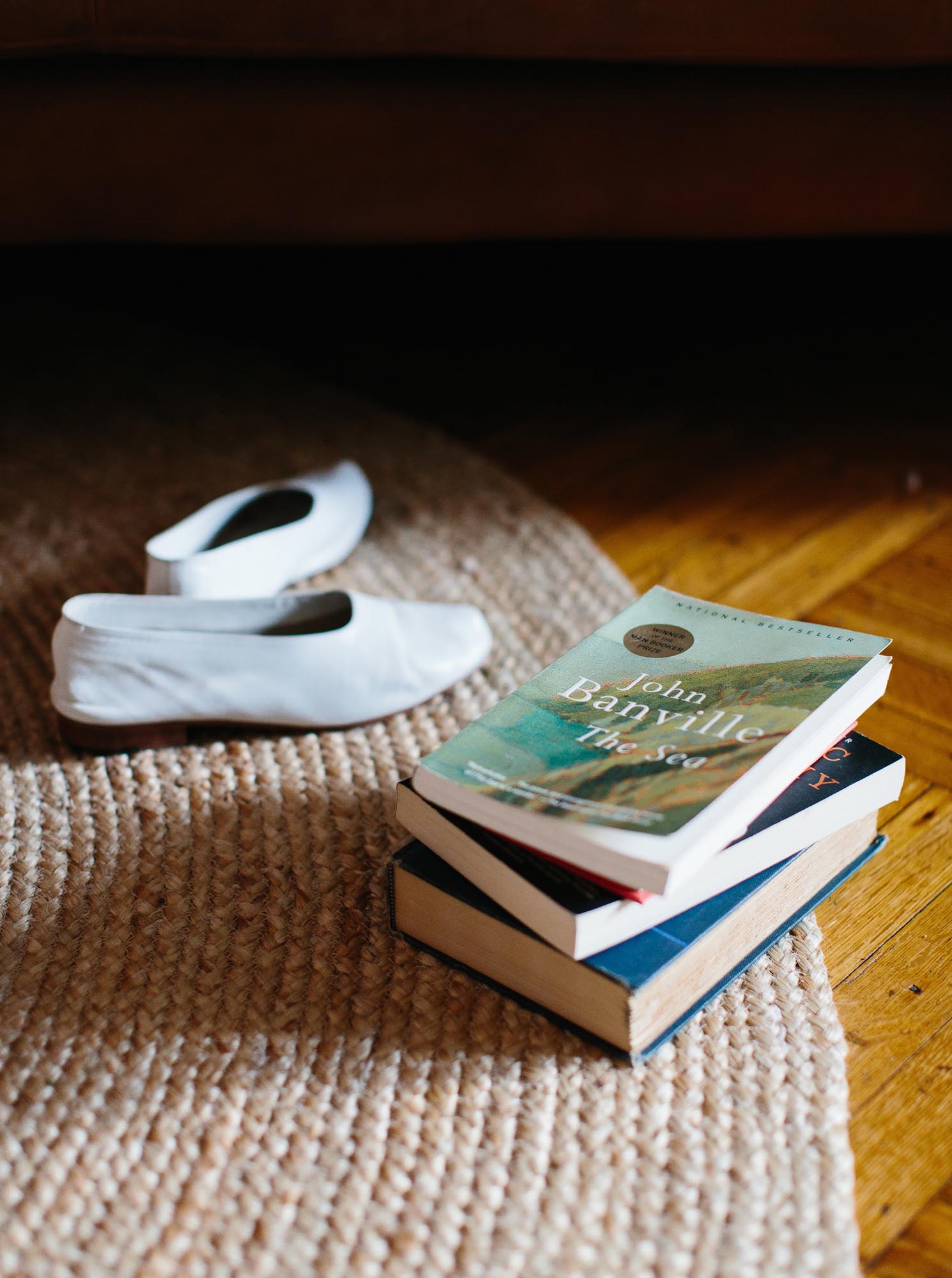 Photo of a short stack of books on a rug with a pair of shoes.