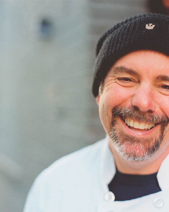 A smiling man in a black beanie hat, sporting a salt-and-pepper goatee