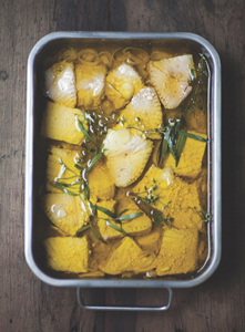 Thick pieces of tuna marinating in oil and herbs in a large metal roasting pan