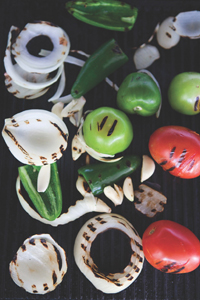 Onion slices, tomato halves, and pepper halves with grill lines piled on a grill