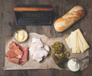 A spread with the fixings for Bob’s Cubano sandwich sitting on a paper bag atop a dark wooden table