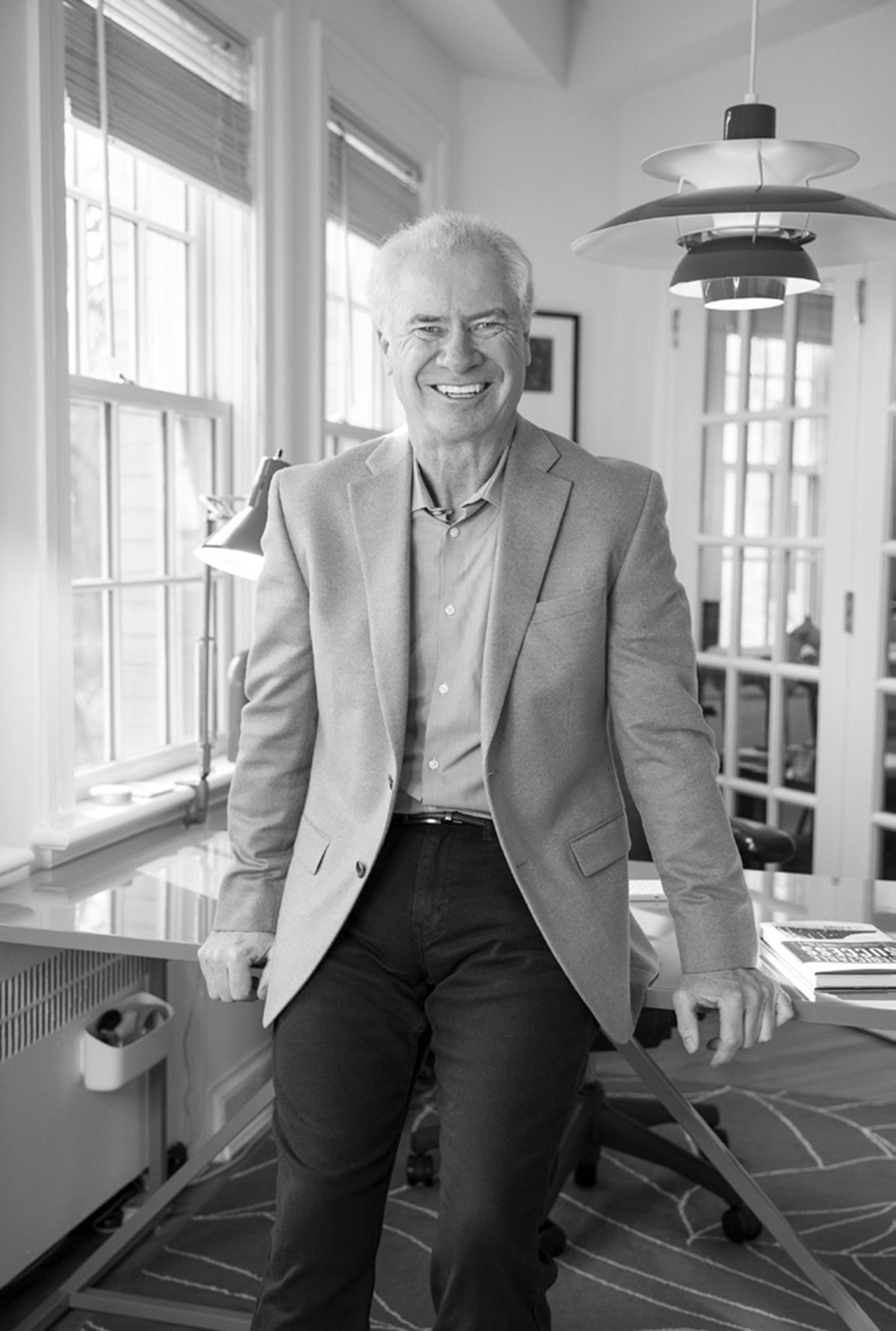 A portait of Lew, smiling whilst perching on his desk.