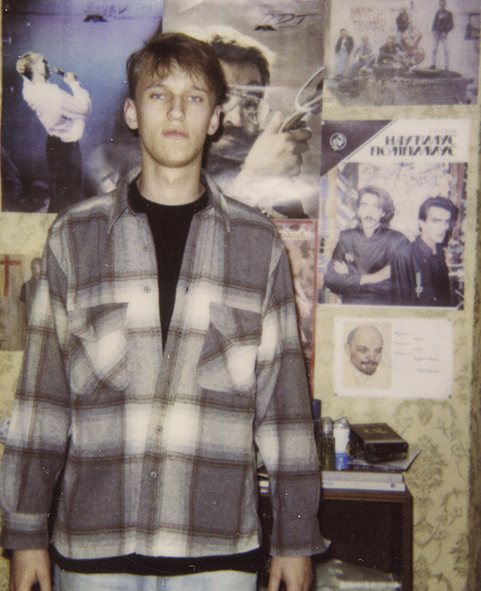 Alexej im Jahr 1992. Er steht im karierten Flanellhemd an der Wand, hinter ihm hängen Poster von russischen Rockbands.