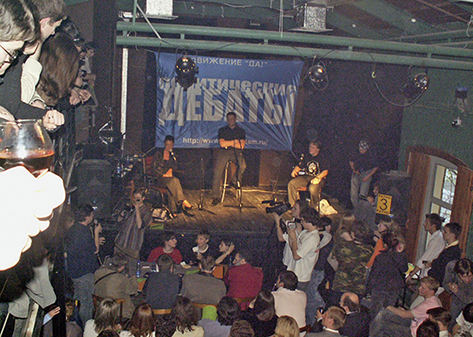 Alexej sitzt auf einem Barhocker auf einer Bühne und moderiert eine politische Debatte in einer Moskauer Bar 2006.