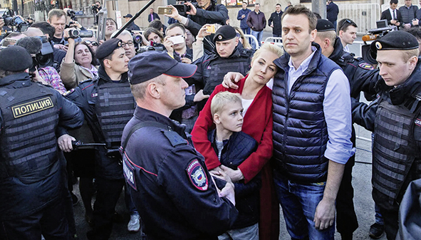 Alexej, Julija und Sachar auf einer Kundgebung in Moskau 2017. Polizeibeamte umstellen das Paar; Alexej hält Julija im Arm, die ihre Arme wiederum um Sachar geschlungen hat. 