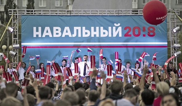 Alexej ist sehr klein auf einer Kundgebung in Omsk während des Präsidentschaftswahlkampfs 2017 in einer Menge aus Köpfen zu sehen. Im Hintergrund ein großes Plakat mit der Aufschrift "Nawalny 2018".