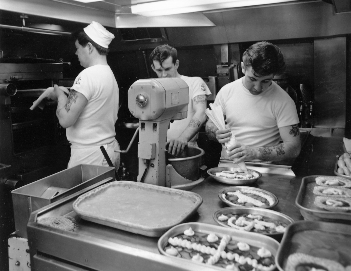 Photograph showing the chefs at work in the kitchen on board the submarine.