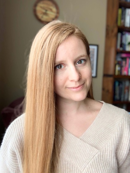 Lauren Connolly headshot. White woman, long red hair, in front of a bookshelf