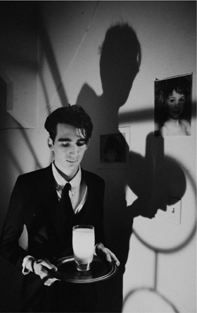 Black and white still of a man carrying a glass of milk on a tray