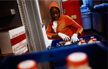 Staff member wearing gloves and a hooded sweatshirt pulling a bottle of milk from a crate