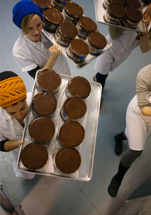 Overhead of kitchen staff carrying layer cakes, eight per tray