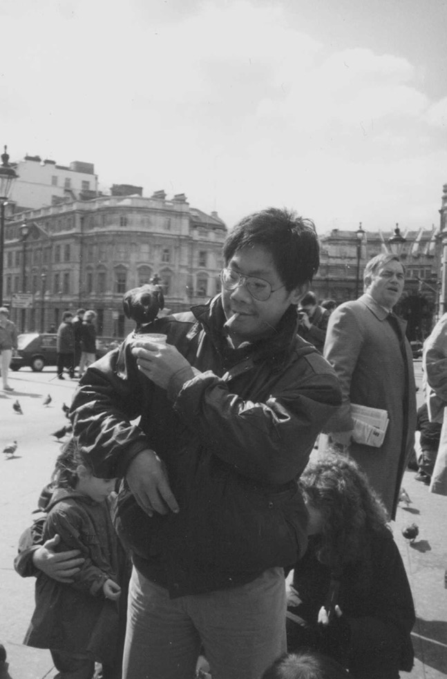 A man with a cigarette in his mouth feeds a pigeon perched on his shoulder