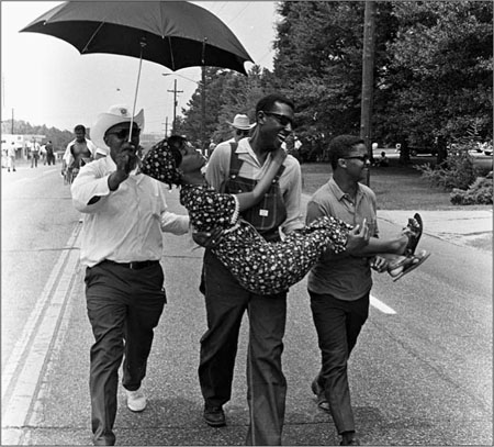 Stokely Carmichael carrying a young woman down the road during the Meredith March in Mississippi. Jim Peppler/ Southern Courier/ Alabama Department of Archives and History, Montgomery, AL.