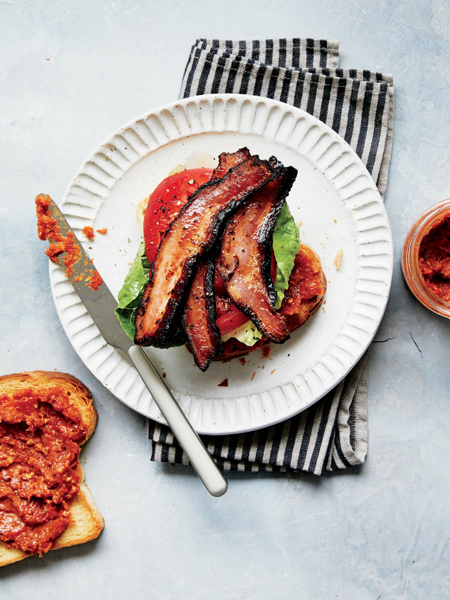 A plate with a BLT sandwich with bacon, roasted tomato, and onion spread.