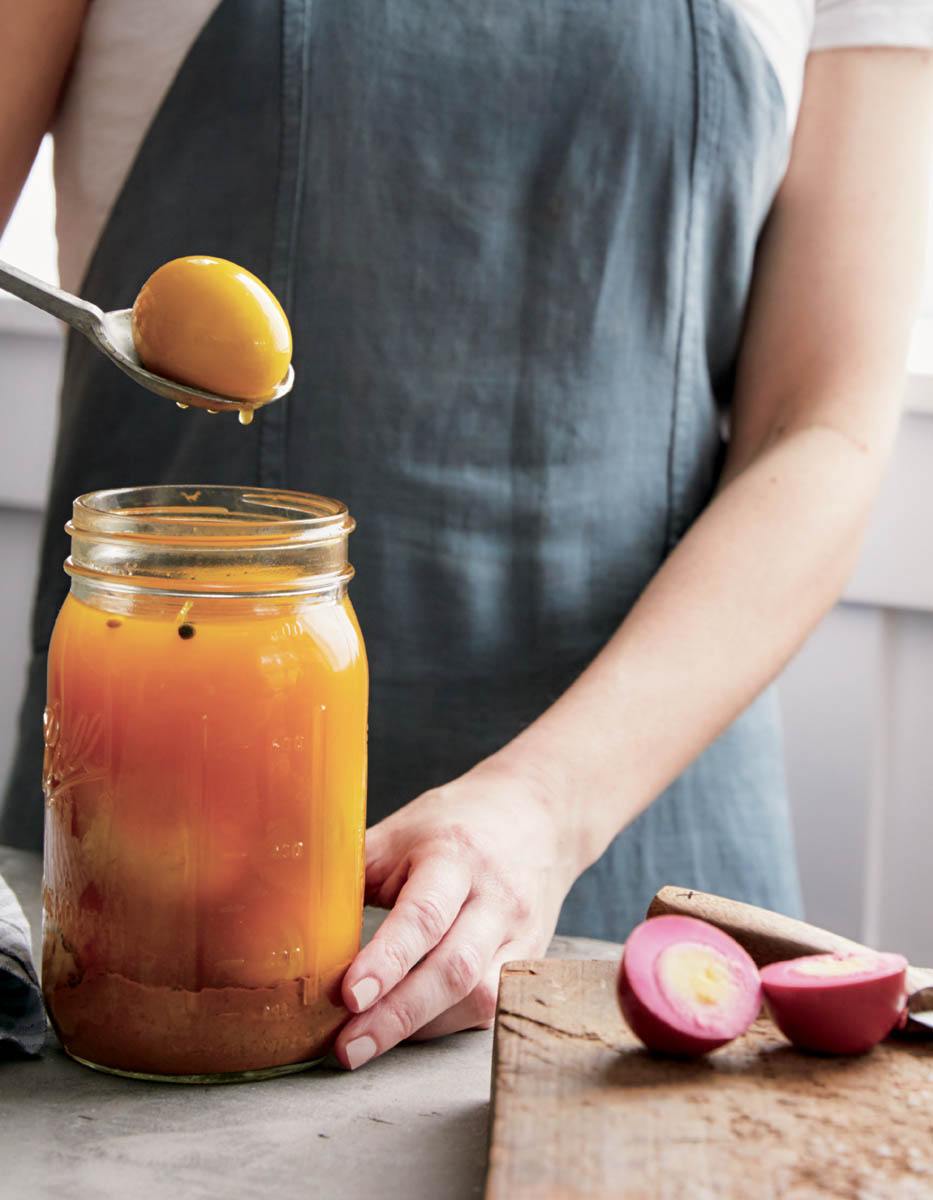 A chef spooning a pickled egg out of a jar.