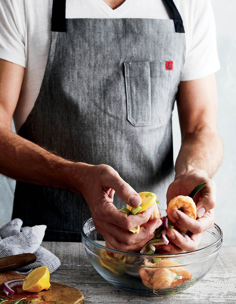 A chef preparing a bowl of shrimp, seasonings, and garnishes.