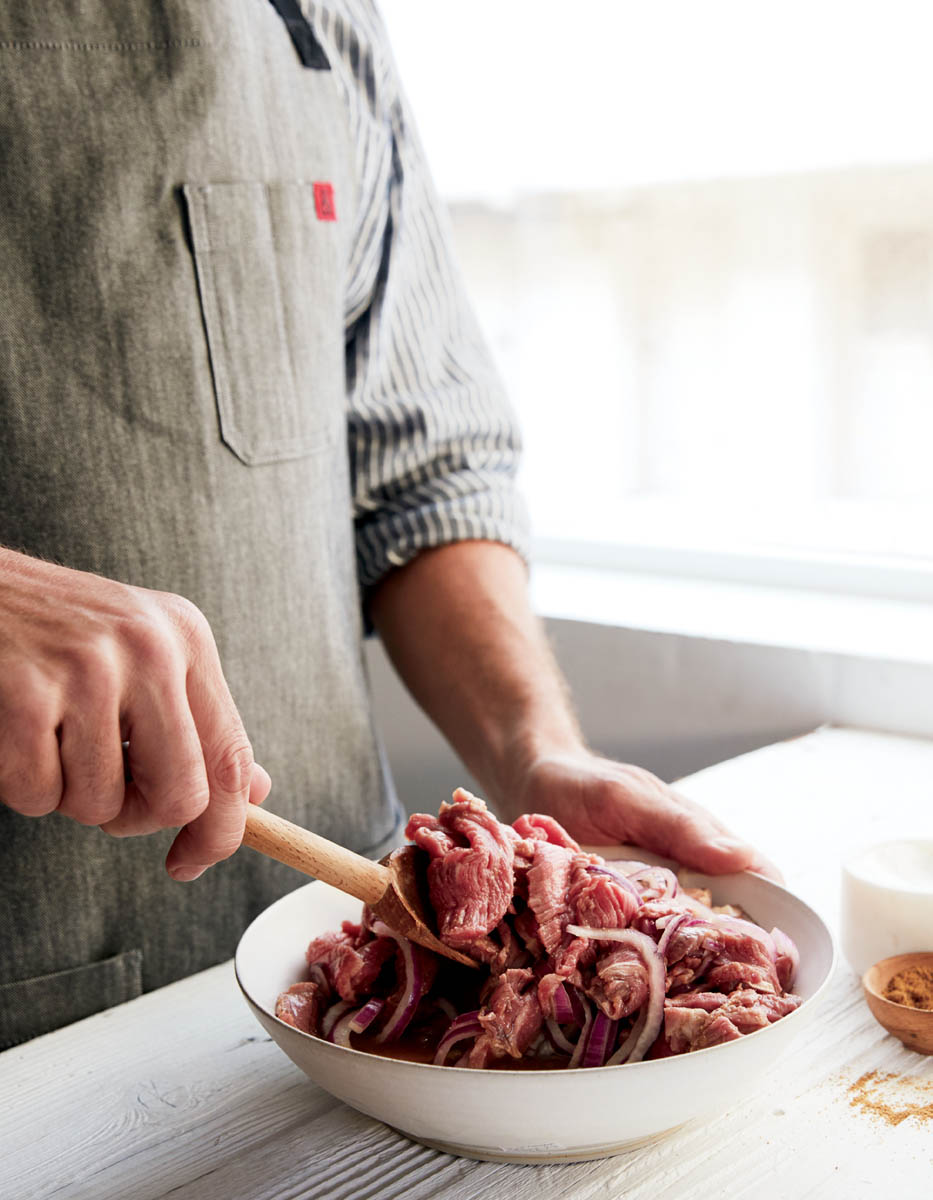 A chef marinading a bowl of beef strips.