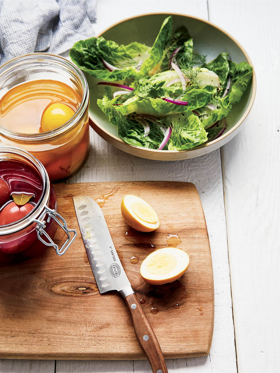 A bowl of salad with jars of curry pickled and beet pickled eggs.