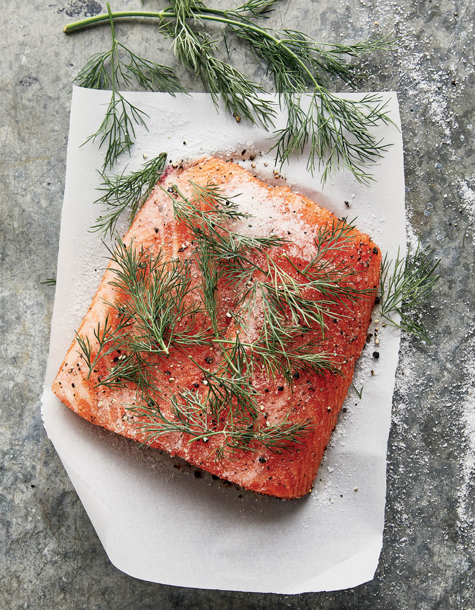 A slice of salmon being dry cured with salt and herbs.