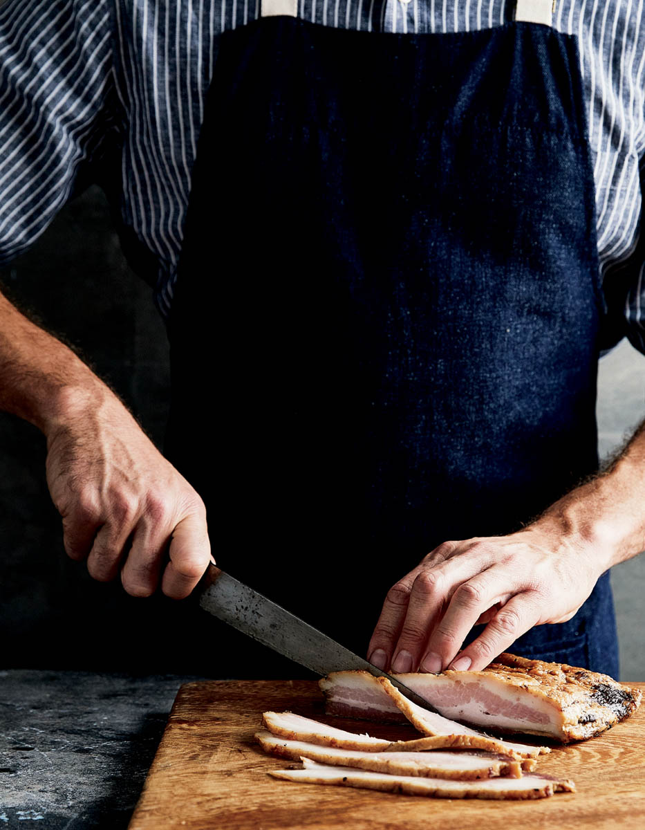 A chef slicing strips of bacon.