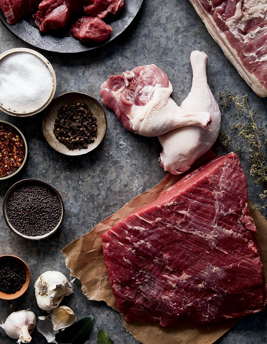 Cuts of uncured meat with a spread of herbs and seasonings.