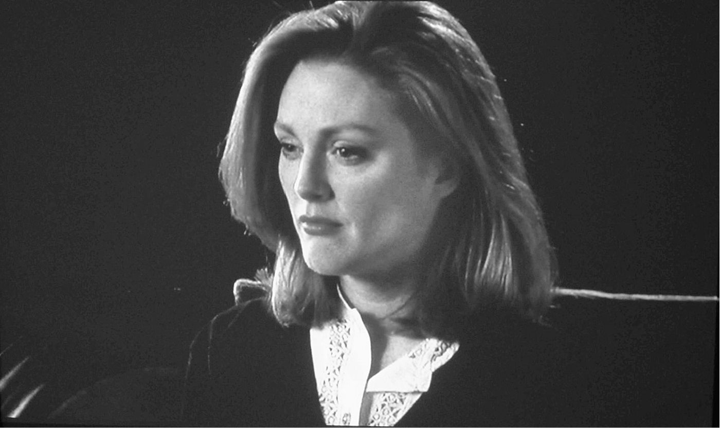 Head shot of a woman who seems displeased, with a dark background.